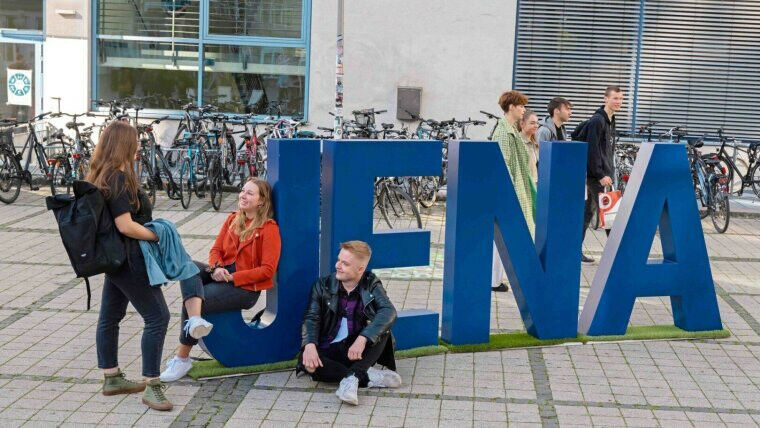 Studierende neben den Buchstaben Jena auf dem Abbe-Campus. Foto: Jens Meyer (Uni